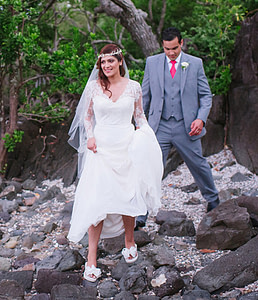 A Bride and Groom carefully walking over rocks to get to the Beach